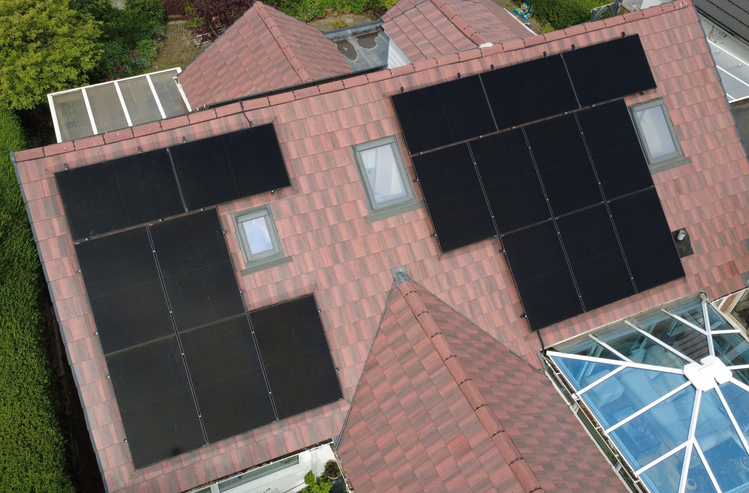 Two arrays set around the roof windows of a red-tiled house, seen from a drone
