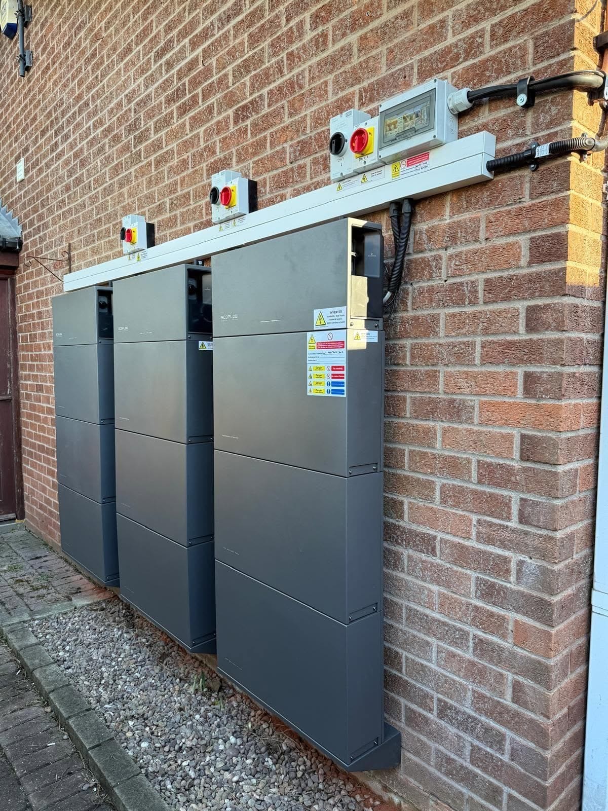 Battery cabinets on an outside brick wall, with isolators and a distribution box on one run of white trunking