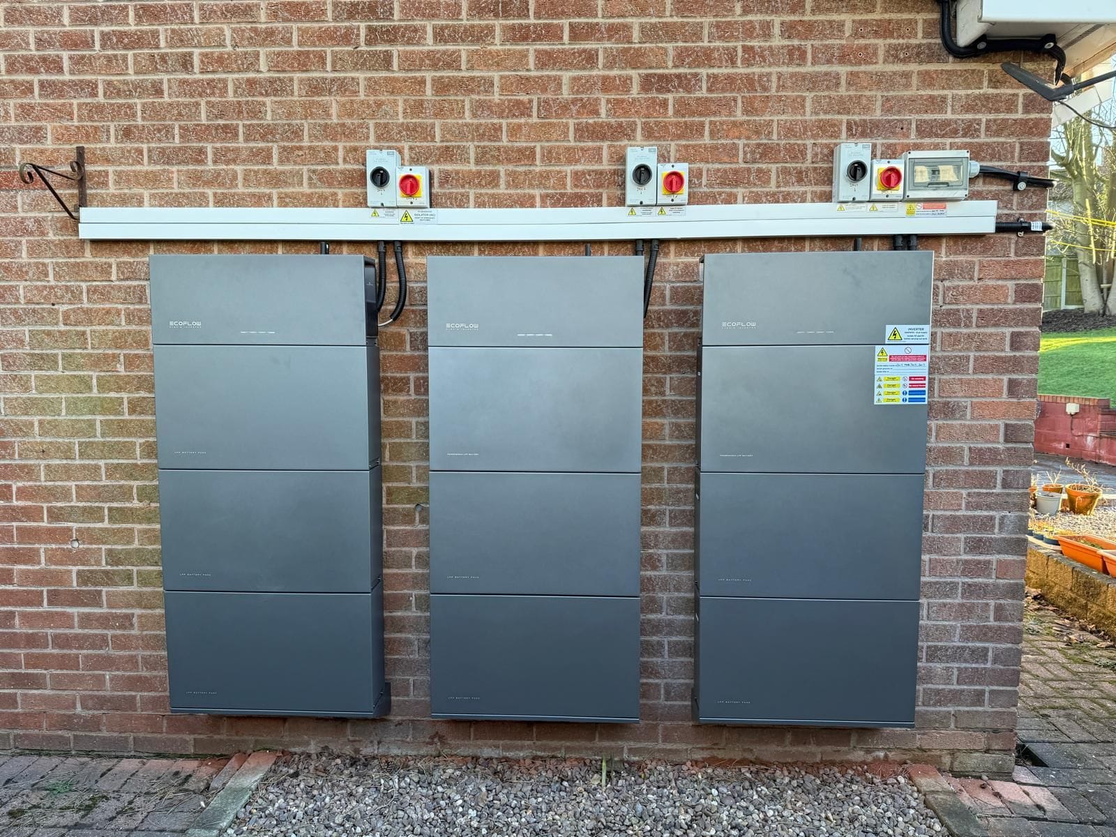 Isolators with warning labels on white trunking above the tops of battery cabinets